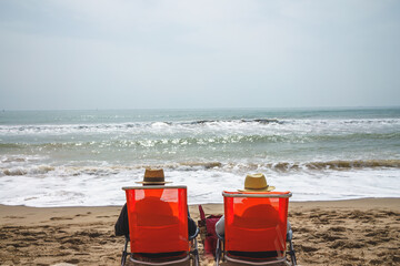 two elderly people on vacation sitting on a deckchair facing the sea