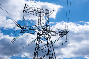 Tower of a high-voltage power line against the of blue sky and clouds