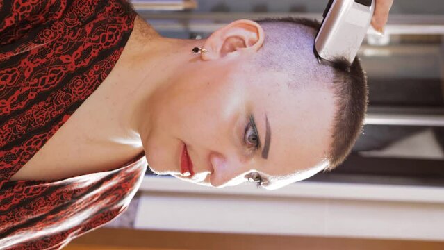 A brunette woman in a bathrobe in the bathroom shaves her head with an electric razor close-up. vertical video