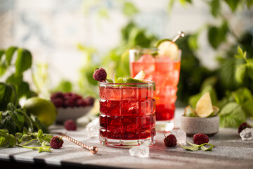Raspberry cocktail with lime,mint,ice cubes and fresh berries on grey background with juicy summer greenery.Beautiful photo of refreshing drink.