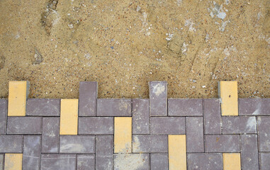 unfinished work on laying paving slabs, after the blocks of yellow and brown, compacted sand...