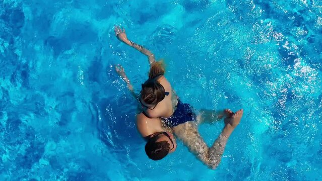 Drone view of a young couple swimming in the pool, enjoying their vacation in a tropical paradise. Two people are resting on vacation, having fun on summer days, sunbathing.
