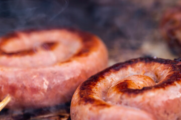 Close up shot of rolled up sausages on skewer placed over barbeque