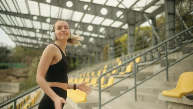 Close up of attractive woman’s smiling face listening music in headphones in the stadium. Portrait of beautiful young woman. High quality 4k footage