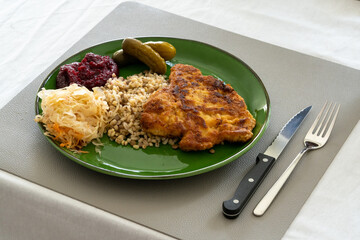 Dinner dish - pork chop with pickled cucumbers, grated beets and bulgur groats, served on a green plate