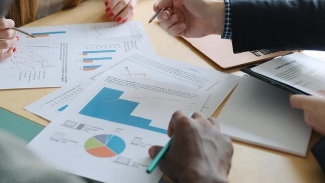Group of unrecognizable business people analyze statistics graphs and diagrams on table. Executives team work with data, checking results of their company. Diverse team multinational, close-up