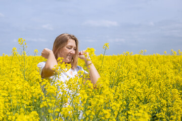Mature fair-haired woman smiling in yellow rapeseed flowers on the field. Summer mood, happy vacation