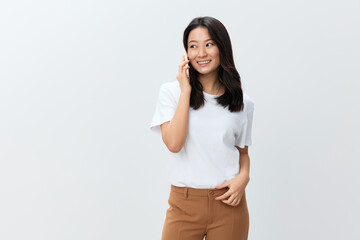 Cheerful cute Asian young female in white basic t-shirt talks with best friend in call using phone posing isolated on over white background. The best offer for ad. People Lifestyle concept. Copy space