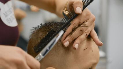 Process of hairdresser cutting hair. Blond caucasian boy is sitting in barber shop and hairdresser...