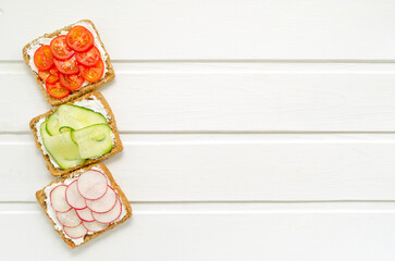 Obraz na płótnie Canvas delicious vegetarian sandwiches with cream cheese, fresh cucumber, radish, tomatoes on a white wooden background. Flat lay. healthy food diet slimming fitness. with place for text. copy space