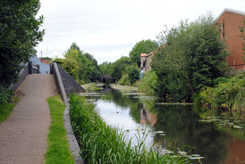 Fototapeta premium Reflections in Calm Waters of Canal with Raised Towpath and Old Mill Building