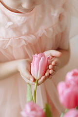 Child girl in a pink dress holds a tulip bud in her hands