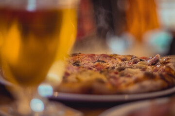 Fresh pizza served on a plate with some vapor rising up, surrounded by glasses of beer. Tasty and...