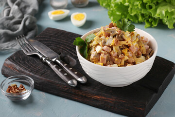 Salad with ham, eggs, onion and champignons in a white bowl on a dark board