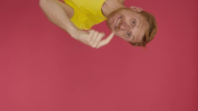 Follow me - Vertical shot view of excited young adult man in yellow shirt stretching arm to camera inviting to follow him - Come here concept with cheerful guy inviting approach over red background