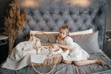 girl taking care of her younger sister on the bed wicker basket pats on the head