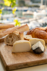 Sunny morning in Provence, breakfast with fresh baked croissants, baquett bread, crottin goat cheese and view on fisherman's boats in harbour of Cassis, Provence, France