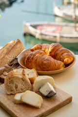 Sunny morning in Provence, breakfast with fresh baked croissants, baquett bread, crottin goat cheese and view on fisherman's boats in harbour of Cassis, Provence, France