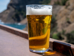 Glass of fresh cold lager beer served outdoor in snack bar with view on Calanque de Figuerolles in...