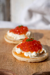 Two small starters blinis with sour cream and salted salmon red caviar served on mango tree wooden...