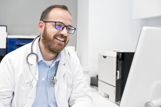 Portrait of friendly smiling healthcare professional therapist sitting at workplace. Happy confident male doctor physician wearing white medical coat and stethoscope. High quality photo