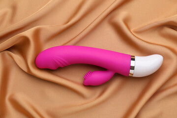 Pink vibrator on golden silk fabric, top view. Sex toy