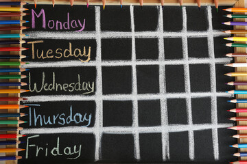Colorful pencils and drawn weekly school timetable on black chalkboard, top view