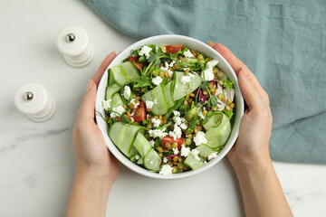 Woman holding bowl of delicious salad with lentils, vegetables and feta cheese at white table, top...