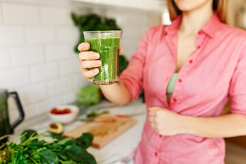 Green smoothie - healthy eating concept. faceless woman holding smoothie shake against kitchen home interior, focus on hands and glass