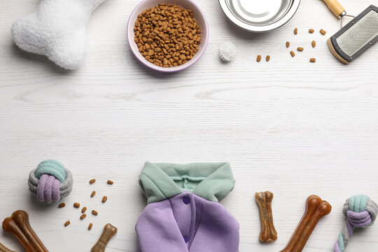 Flat lay composition with dog clothes, food and accessories on white wooden table. Space for text