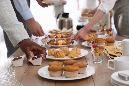 People near table with different delicious snacks during coffee break, closeup