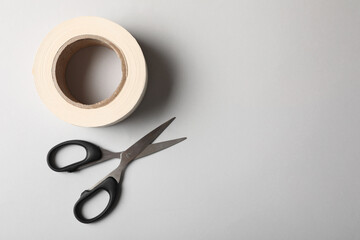 Roll of adhesive tape and scissors on light background, top view. Space for text