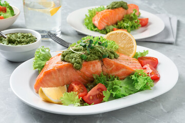 Tasty cooked salmon with pesto sauce and fresh salad served on grey table