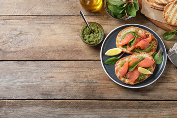 Delicious bruschettas with salmon and pesto sauce on wooden table, flat lay. Space for text