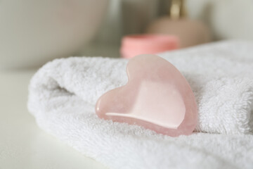 Rose quartz gua sha tool with soft towel on white table, closeup