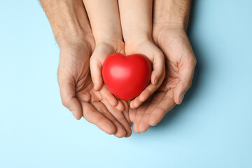 Man and kid holding red heart in hands on light blue background, top view