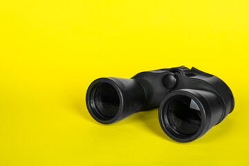 Modern binoculars on yellow background, space for text