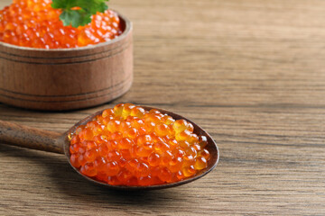 Spoon and bowl with delicious red caviar on wooden table, closeup. Space for text