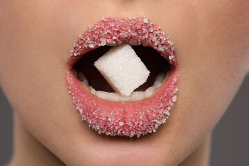 Woman with beautiful lips eating sugar cube on grey background, closeup