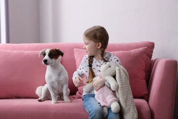Cute little girl with her dog and toy bunny on sofa indoors. Childhood pet - Powered by Adobe