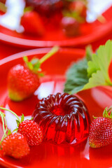 Strawberry Berry jelly.Low calorie diet dessert.Red jelly and strawberries with green leaves on a red plate on a Red background.Healthy natural sweets and desserts. 