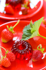 Strawberry jelly.Berry jelly.Low calorie dessert.Red jelly and strawberries with green leaves on a red plate on a Red background.Healthy natural sweets and desserts. 