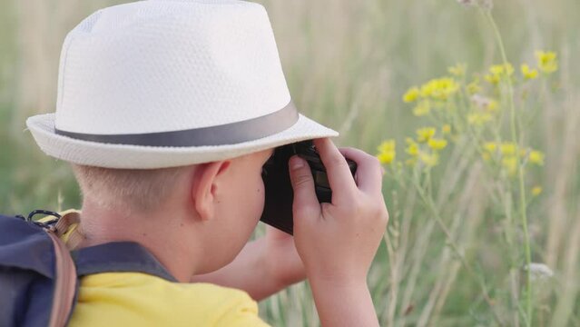 Child dreams of traveling, making discoveries. Child boy plays with camera, photographs flowers in summer park. Concept of childrens fantasy in nature. Happy boy, child dreams of becoming photographer
