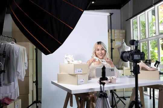 Young attractive Asian female blogger or vlogger looking at camera reviewing product. Modern businesswoman using social media for marketing. Business online influencer on social media concept.