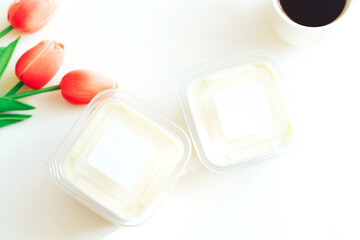 Bird's milk in plastic containers next to coffee and tulips.