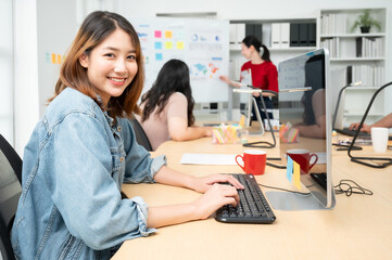 Young asian beautiful woman working on computer at workplace with a business team group