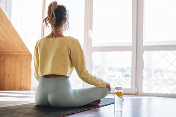Young sllim fitness blonde woman practice morning yoga near the window of home