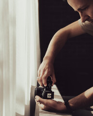 Young man is taking photo with camera near the window in sunny day.