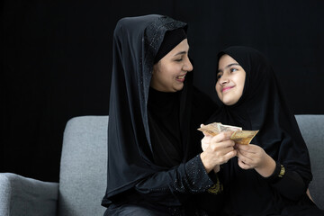 muslim woman or mother giving cash money to her daughter on black background