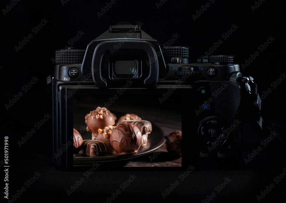 Wall mural dslr camera or mirrorless body lit by a rim light showing chocolates on the back of the camera displ